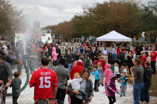 A lively outdoor event with families and children enjoying foam, games, and festivities under cloudy skies.