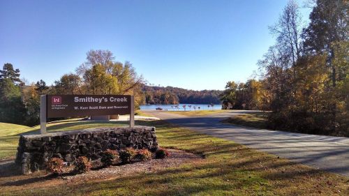 Sign for Smithey's Creek at Kerr Scott Dam and Reservoir, with a scenic view of the water and trees in the background.