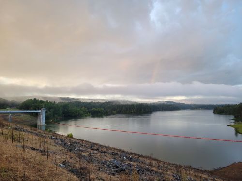 A serene lake surrounded by trees under a cloudy sky, with a hint of a rainbow in the distance.