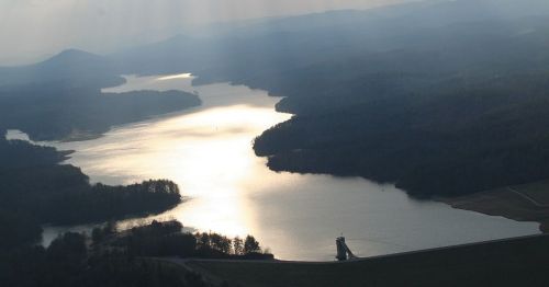 Aerial view of a serene lake surrounded by mountains, with sunlight reflecting on the water's surface.
