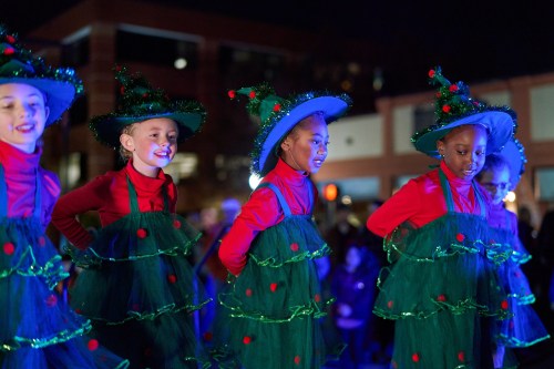 A group of children in festive costumes resembling Christmas trees perform at a nighttime event.
