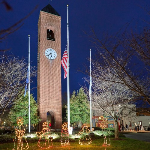A clock tower at night, adorned with holiday lights, surrounded by trees and festive decorations.