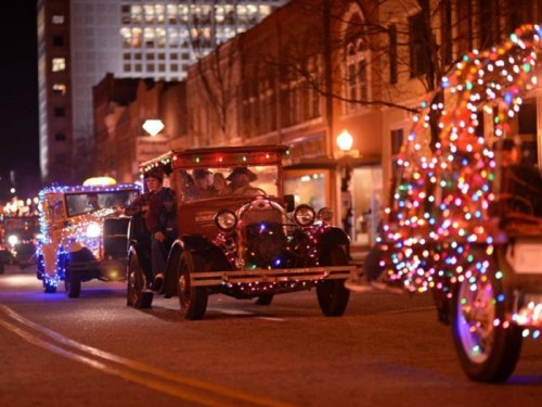 A festive parade of vintage cars adorned with colorful Christmas lights at night.