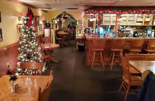 Cozy restaurant interior decorated for the holidays, featuring a Christmas tree and wooden tables.