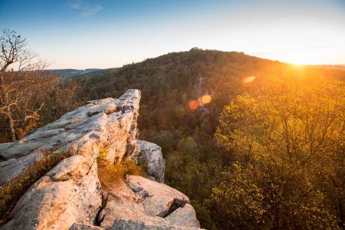 Sunset over a rocky cliff with lush green hills in the background, casting warm golden light across the landscape.