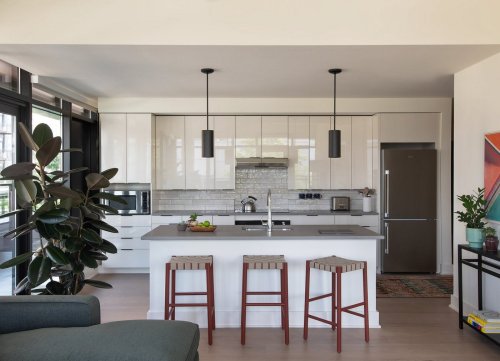 Modern kitchen with white cabinets, gray island, three wooden stools, and large windows letting in natural light.