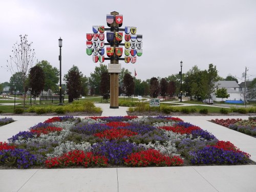 A colorful flower bed in a park, featuring a central monument with various coats of arms and flags.