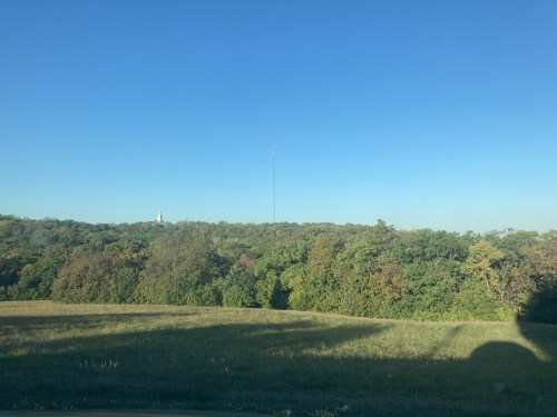 A clear blue sky over a green hillside with a tall radio tower in the distance.