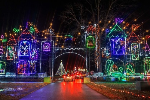 Colorful holiday lights illuminate a castle archway, with a decorated tree and festive displays in the background.