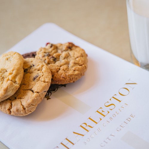 A city guide for Charleston, South Carolina, with three cookies and a glass of milk beside it.