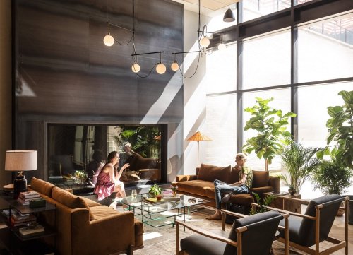 A modern living room with large windows, plants, and stylish furniture. Two people are seated, enjoying the space.