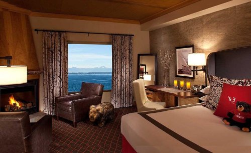 Cozy hotel room with a view of the ocean, featuring a bed, armchair, desk, and decorative elements.