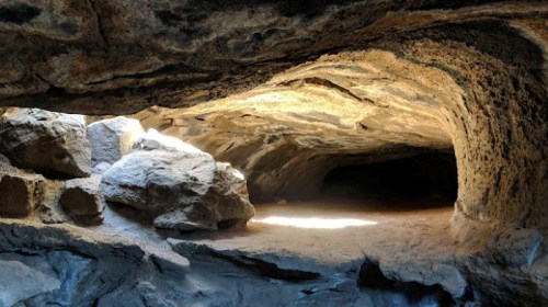 A rocky cave interior with sunlight illuminating the entrance and shadows in the background.