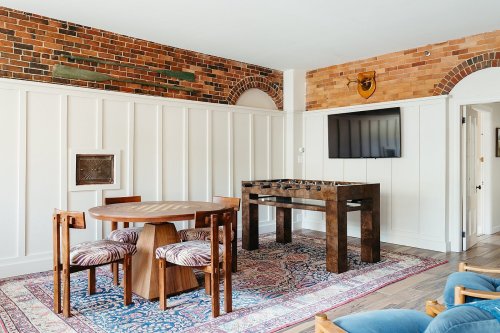 A stylish room featuring a round dining table, foosball table, and brick walls with decorative accents.