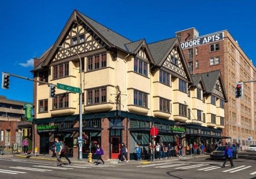 Historic building at a street corner with shops below and pedestrians walking by, under a clear blue sky.