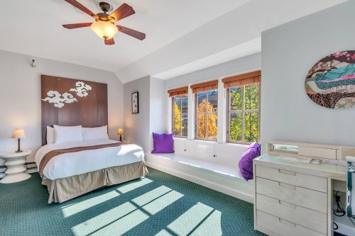Bright bedroom with a bed, window seat, and decorative wall art, featuring natural light and autumn views outside.