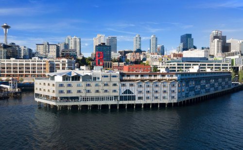 A waterfront building with a modern design, surrounded by city skyscrapers and a clear blue sky.
