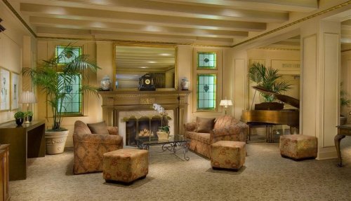 Cozy lounge with a fireplace, plush seating, piano, and decorative plants in a warm, inviting atmosphere.
