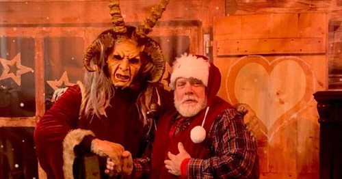 A man dressed as Krampus poses with Santa Claus in a festive setting, both wearing holiday attire.
