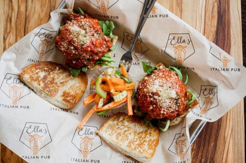 Two meatball sandwiches on toasted bread, served with a side of pickled vegetables, on branded parchment paper.