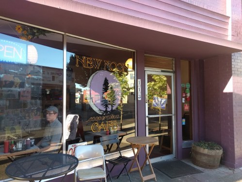 A cozy café entrance with a sign reading "New Moon Cooperative Café" and outdoor seating.