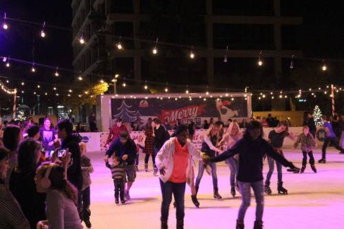 A lively outdoor ice skating rink at night, decorated with festive lights and people skating joyfully.