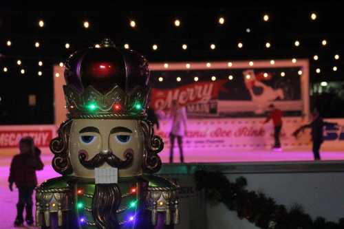 A brightly lit nutcracker statue in the foreground with people ice skating in the background, decorated with string lights.