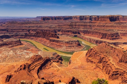 A vast canyon landscape with red rock formations and a winding river under a clear blue sky.