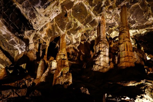 Stalactites and stalagmites illuminated in a dark cave, showcasing unique rock formations and textures.