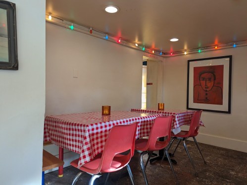A cozy dining area with a checkered tablecloth, red chairs, and colorful string lights on the walls.