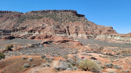 A rugged landscape featuring layered red rock formations and sparse vegetation under a clear blue sky.