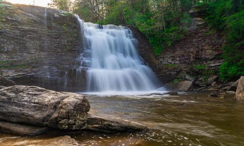 A serene waterfall cascades over rocky cliffs into a calm pool, surrounded by lush greenery.