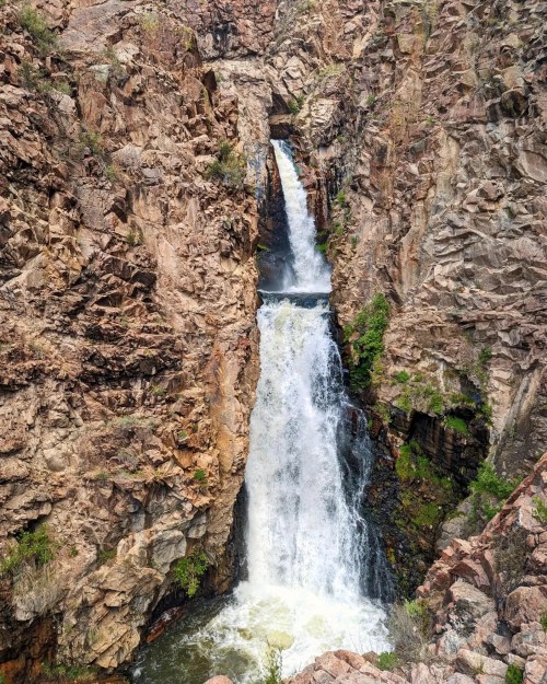 A stunning waterfall cascading between rocky cliffs, surrounded by lush greenery and rugged terrain.
