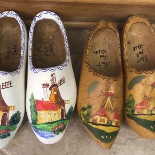 Two pairs of decorative wooden clogs, one white with colorful windmill designs and one brown with similar artwork.