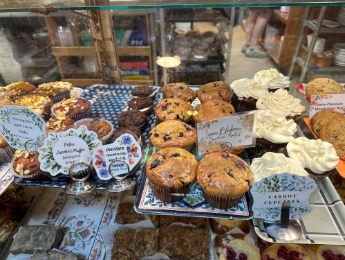 A display case filled with various baked goods, including muffins, cupcakes, and brownies, with decorative labels.