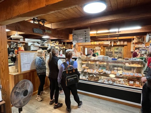 A cozy bakery interior with customers lined up at the counter, showcasing a variety of baked goods in display cases.