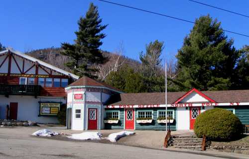 A quaint, colorful building with red doors and windows, surrounded by trees and snow, under a clear blue sky.