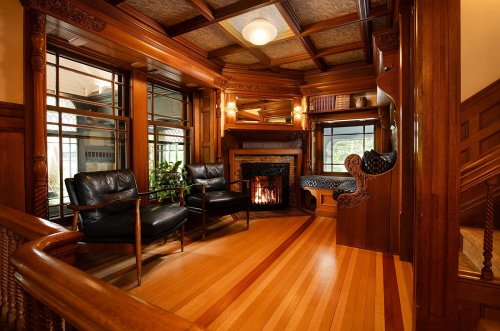 Cozy wooden interior with two black chairs, a fireplace, and intricate architectural details. Warm and inviting atmosphere.