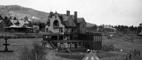 Historic black-and-white photo of a large, ornate mansion surrounded by trees and mountains.