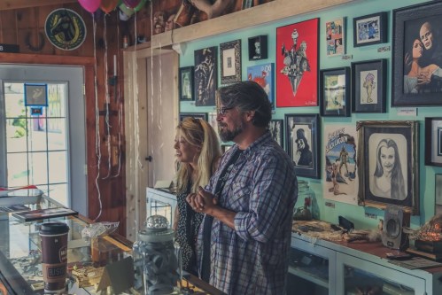 A man and woman stand in a gallery filled with framed artwork and decorations, smiling at the camera.