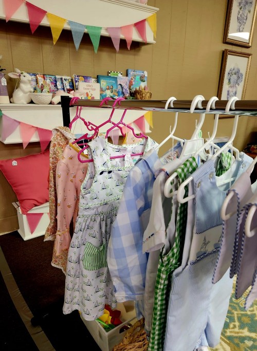A display of colorful children's clothing on hangers, with a backdrop of decorative bunting and books.