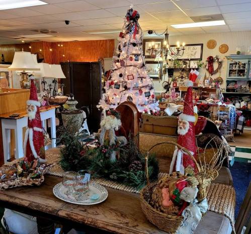 A cozy shop display featuring a decorated Christmas tree, festive decorations, and holiday-themed figurines on a wooden table.