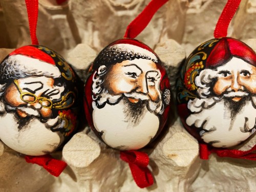 Three hand-painted Christmas ornaments featuring Santa Claus faces, each with unique expressions and red ribbons.