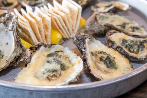 A platter of baked oysters topped with cheese, served with lemon wedges and crackers.
