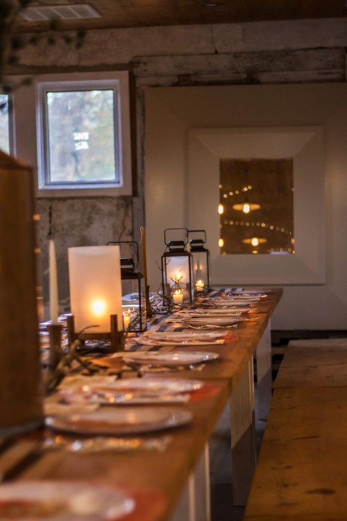 A beautifully set dining table with candles and lanterns, creating a warm, inviting atmosphere in a rustic space.