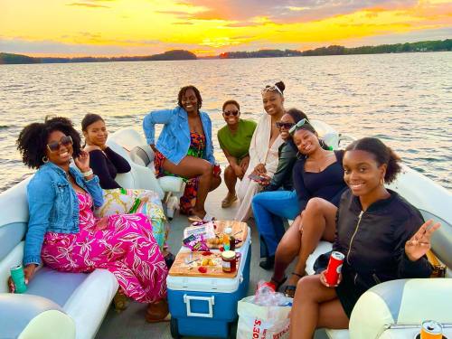 A group of eight women enjoying a sunset on a boat, smiling and posing together with snacks and drinks.