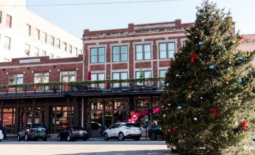 A festive street scene featuring a decorated Christmas tree and a brick building adorned with holiday decorations.