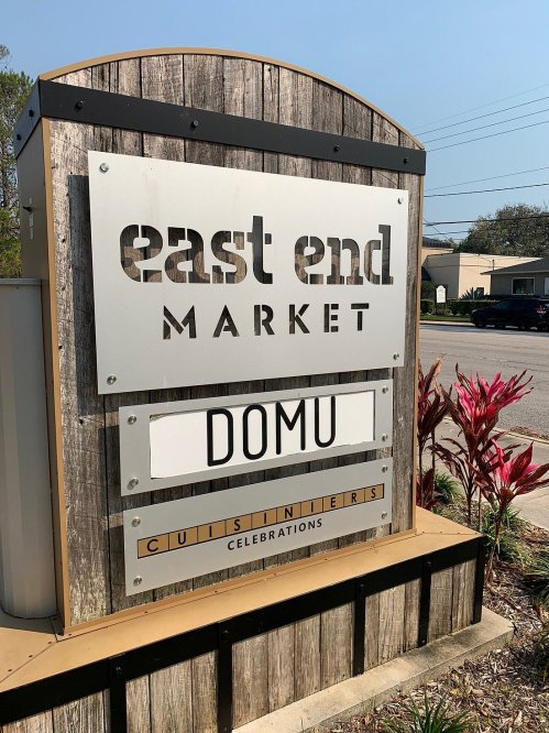 Sign for East End Market featuring the name "DOMU" with decorative plants in the foreground.