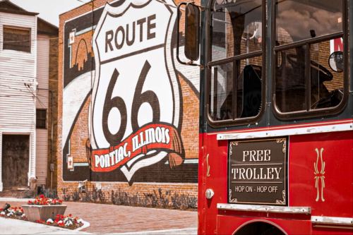 A red trolley in front of a large mural depicting Route 66 in Pontiac, Illinois.