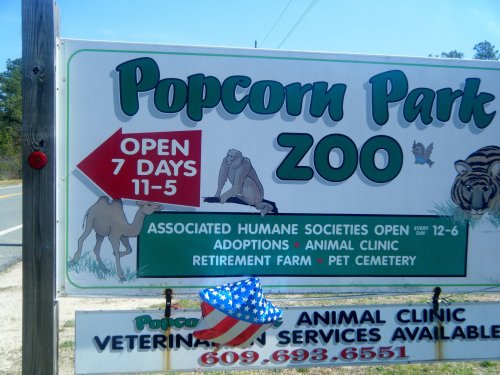 Sign for Popcorn Park Zoo, open 7 days a week, featuring animal clinic, adoptions, and pet cemetery services.